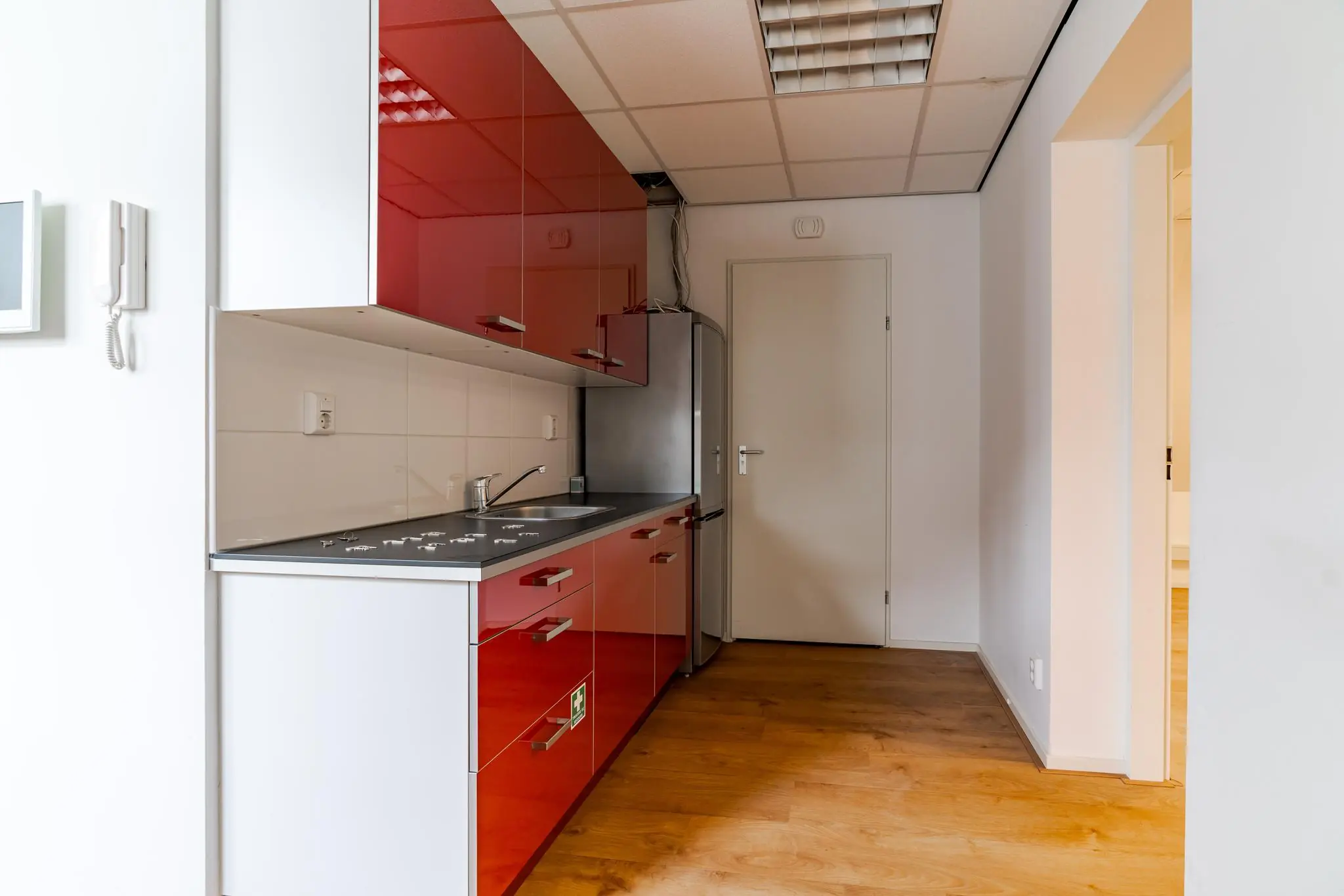 Moderne kitchenette met rode hoogglans kastjes, een roestvrijstalen koelkast en houten vloer in een appartement aan het Lange Voorhout.